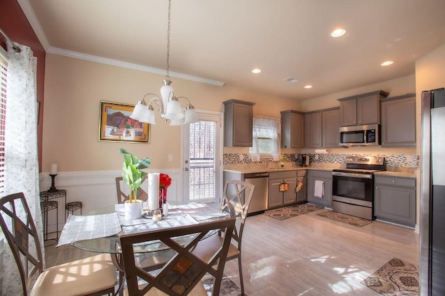 kitchen with stainless steel appliances, crown molding, gray cabinetry, and decorative light fixtures