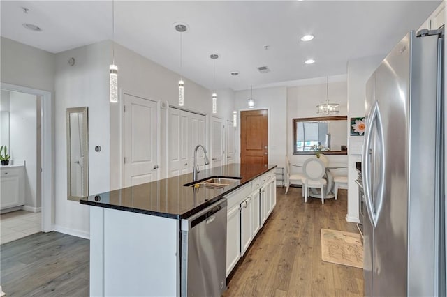 kitchen with a center island with sink, wood finished floors, stainless steel appliances, white cabinetry, and a sink