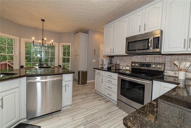 8601 Flint Hill Rd, Douglasville, GA 30135 - kitchen with appliances with stainless steel finishes, white cabinetry, a chandelier, backsplash, and dark stone countertops