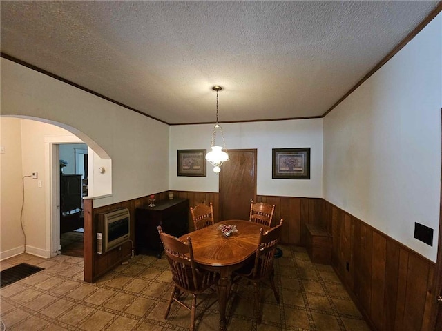 dining space with a textured ceiling, wood walls, ornamental molding, and heating unit