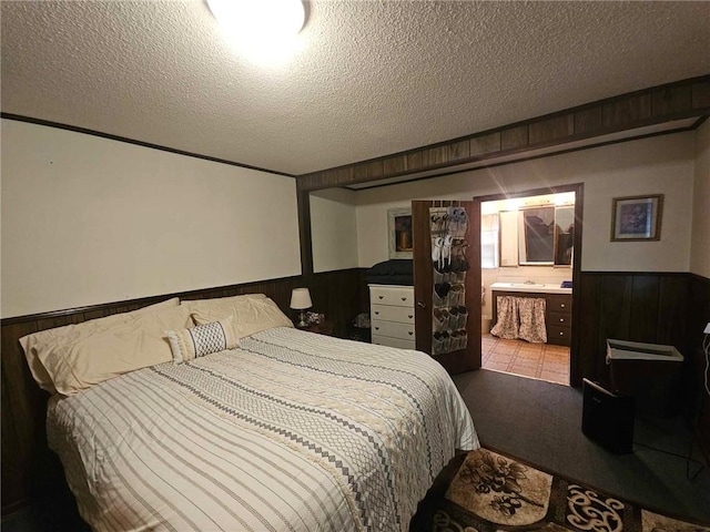 bedroom with a textured ceiling, wood walls, and ensuite bathroom