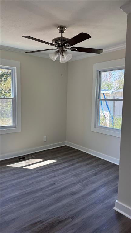 empty room featuring baseboards, ornamental molding, a ceiling fan, and dark wood-style floors
