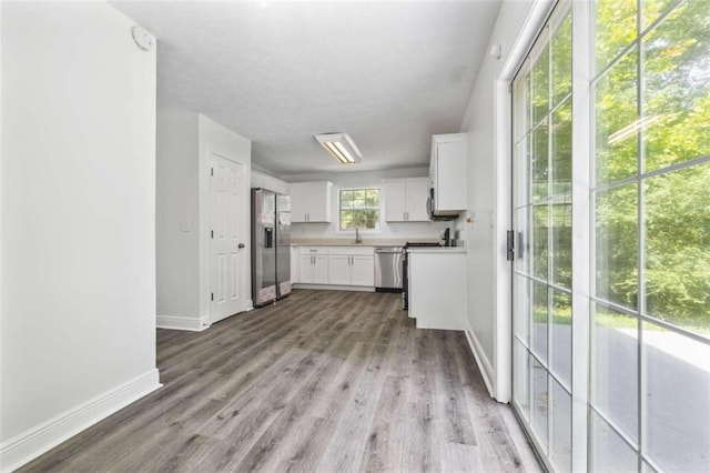 kitchen featuring appliances with stainless steel finishes, plenty of natural light, light hardwood / wood-style floors, and white cabinetry