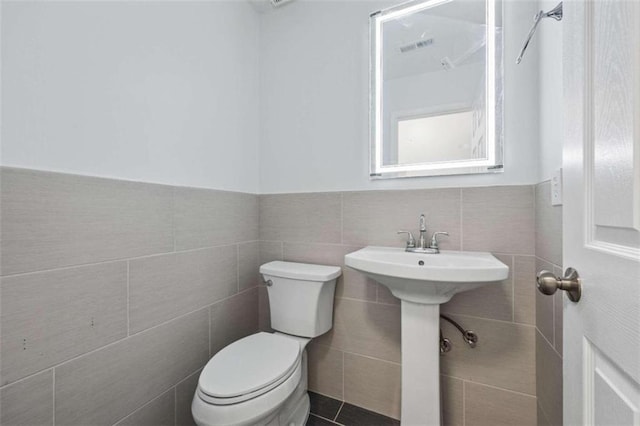 bathroom with tile patterned flooring, tile walls, toilet, and decorative backsplash