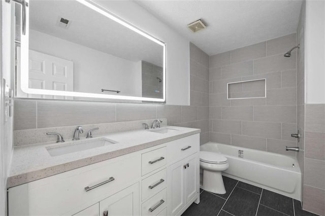 full bathroom with tiled shower / bath, double vanity, tile patterned flooring, tile walls, and toilet