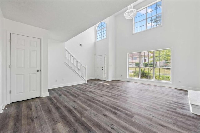 unfurnished living room with dark hardwood / wood-style flooring, an inviting chandelier, and a towering ceiling