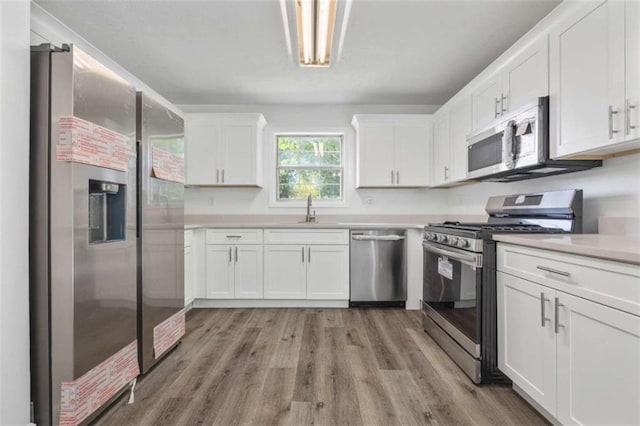 kitchen featuring appliances with stainless steel finishes, light hardwood / wood-style flooring, white cabinetry, and sink