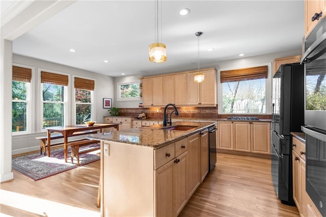 kitchen with sink, decorative light fixtures, a center island with sink, light brown cabinets, and light stone countertops