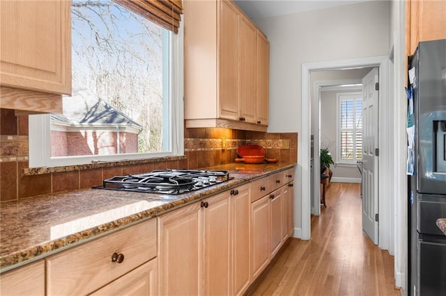 kitchen with tasteful backsplash, light stone counters, stainless steel appliances, light brown cabinets, and light hardwood / wood-style flooring