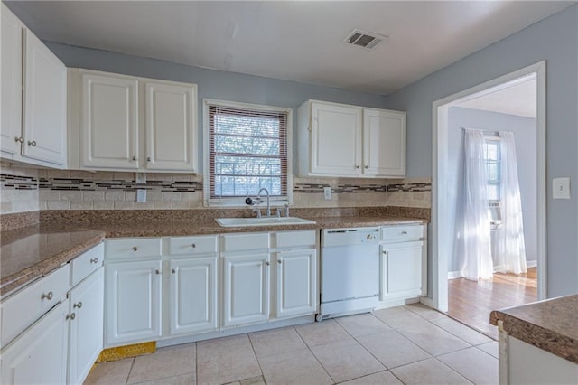 kitchen featuring decorative backsplash, white dishwasher, sink, light tile patterned floors, and white cabinets