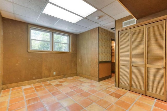 basement featuring light tile patterned flooring, wood walls, and a drop ceiling