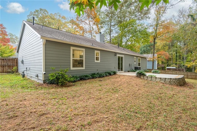 rear view of house featuring a patio area, a chimney, a yard, and fence