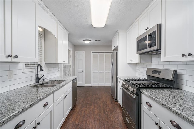 kitchen with dark wood-type flooring, light stone countertops, appliances with stainless steel finishes, white cabinetry, and a sink