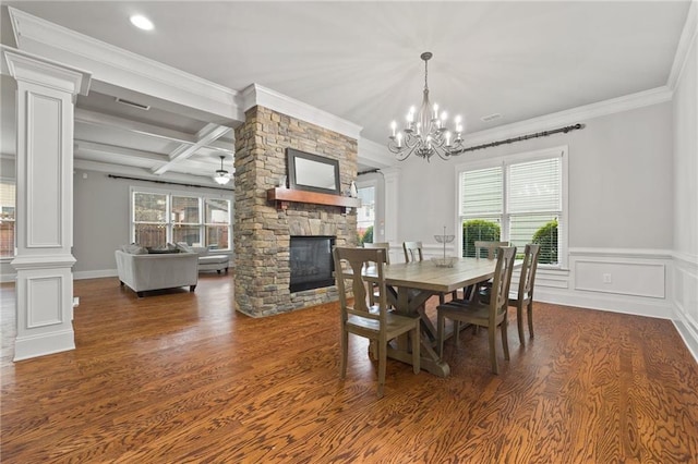 dining room featuring beam ceiling, coffered ceiling, wood finished floors, a stone fireplace, and ornate columns