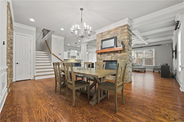 dining space featuring wood finished floors, ornamental molding, a stone fireplace, stairs, and a chandelier