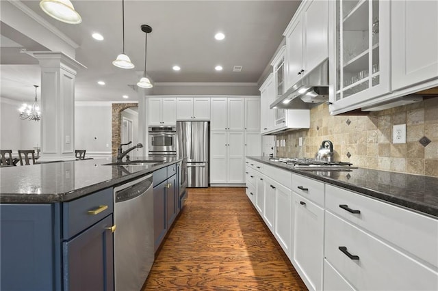 kitchen with a sink, under cabinet range hood, white cabinetry, appliances with stainless steel finishes, and decorative columns