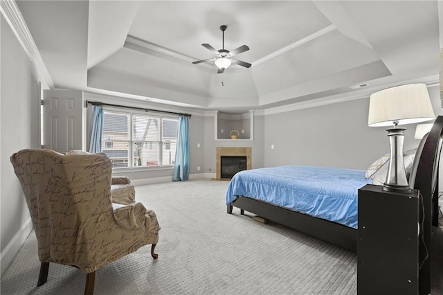 carpeted bedroom with a ceiling fan, baseboards, ornamental molding, a tiled fireplace, and a raised ceiling