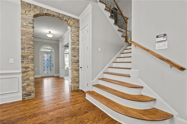 entryway featuring wood finished floors, arched walkways, ornamental molding, and stairs