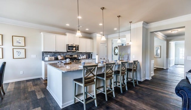 kitchen featuring a breakfast bar area, appliances with stainless steel finishes, stone counters, pendant lighting, and white cabinets