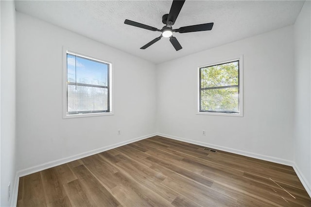 spare room featuring plenty of natural light, visible vents, wood finished floors, and baseboards
