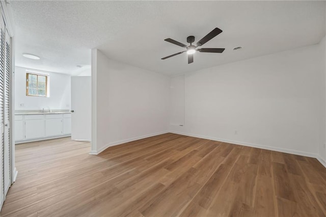 empty room featuring a sink, visible vents, light wood finished floors, ceiling fan, and baseboards