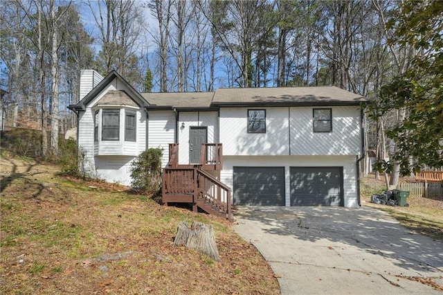 raised ranch featuring fence, concrete driveway, a garage, and a chimney