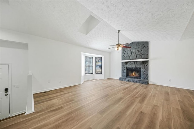 unfurnished living room featuring a textured ceiling, baseboards, ceiling fan, a fireplace, and light wood-type flooring