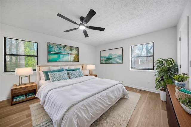 bedroom featuring a textured ceiling, visible vents, light wood finished floors, ceiling fan, and baseboards