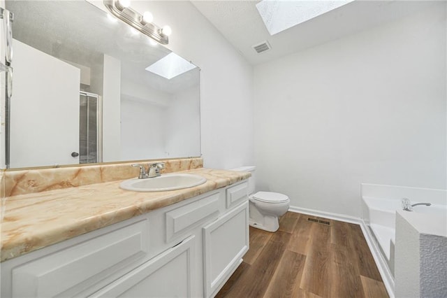 bathroom with toilet, wood finished floors, a skylight, a shower stall, and vanity