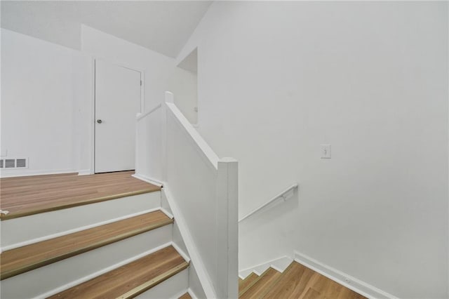 staircase with baseboards, visible vents, and wood finished floors