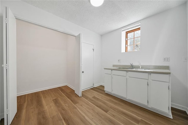 interior space featuring a textured ceiling, a sink, white cabinetry, light wood-style floors, and light countertops