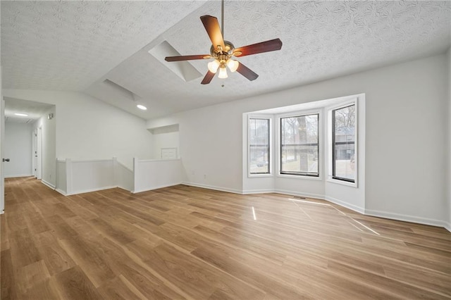 unfurnished living room featuring a ceiling fan, light wood-style flooring, a textured ceiling, and vaulted ceiling