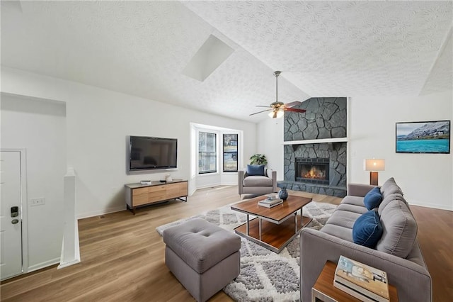 living area with baseboards, a stone fireplace, ceiling fan, and wood finished floors