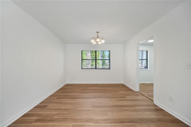 unfurnished room featuring plenty of natural light, a chandelier, baseboards, and light wood-style floors