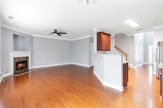 unfurnished living room featuring ceiling fan, a high end fireplace, wood-type flooring, and ornamental molding