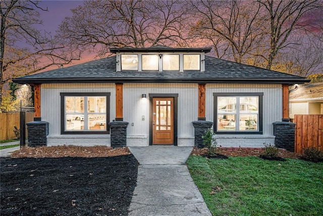 view of front of home featuring brick siding, fence, and roof with shingles