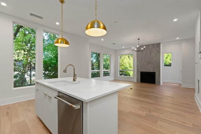 kitchen featuring decorative light fixtures, an island with sink, sink, white cabinets, and stainless steel dishwasher