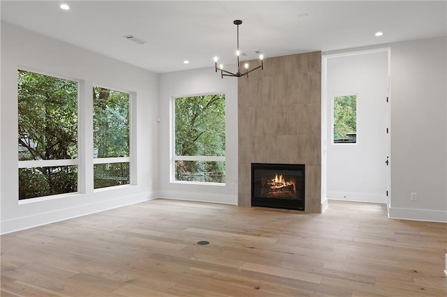 unfurnished living room featuring a tiled fireplace, light hardwood / wood-style flooring, and a chandelier