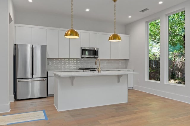 kitchen featuring white cabinetry, backsplash, an island with sink, and appliances with stainless steel finishes