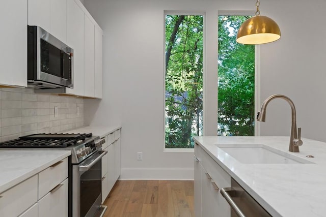 kitchen with tasteful backsplash, sink, white cabinets, stainless steel appliances, and light stone countertops