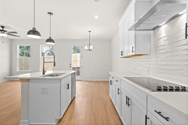 kitchen with a kitchen island with sink, wall chimney range hood, oven, and hanging light fixtures