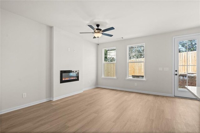 unfurnished living room with a large fireplace, ceiling fan, and light wood-type flooring