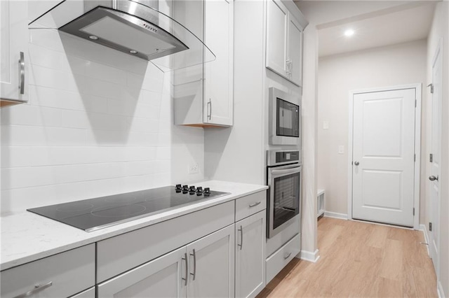 kitchen featuring wall chimney exhaust hood, light stone countertops, light wood-type flooring, and black appliances