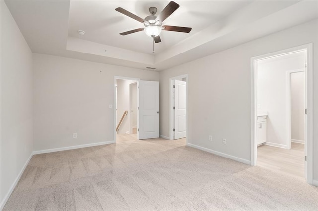 unfurnished bedroom featuring light carpet, a tray ceiling, and ensuite bath