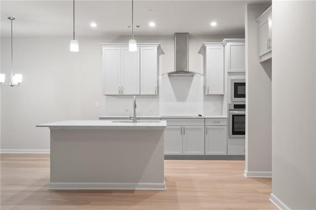 kitchen featuring hanging light fixtures, a kitchen island with sink, wall chimney range hood, and oven