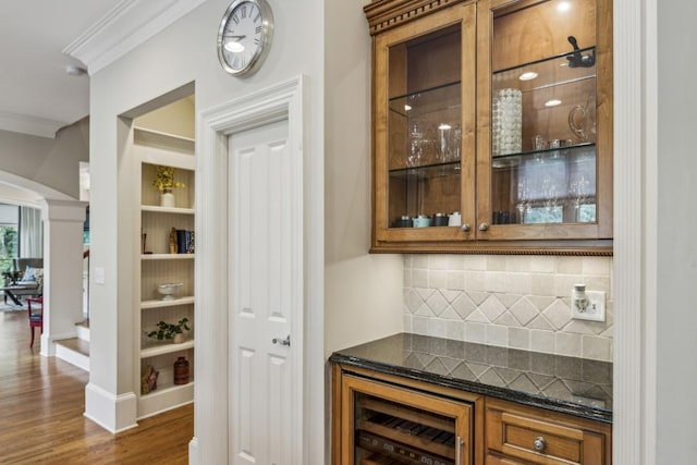 bar area with crown molding, tasteful backsplash, arched walkways, wood finished floors, and decorative columns