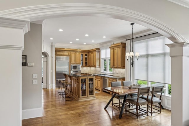 dining area featuring arched walkways, a chandelier, ornamental molding, light wood-type flooring, and plenty of natural light