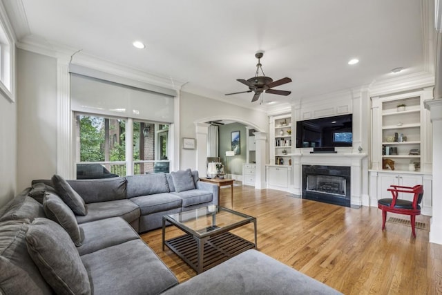living room featuring arched walkways, a ceiling fan, crown molding, a fireplace, and recessed lighting