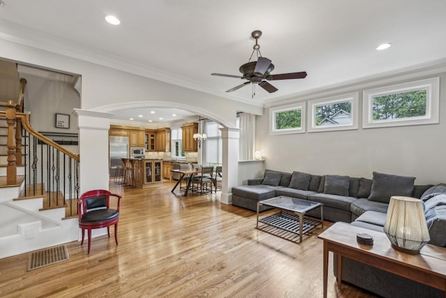 living area with a ceiling fan, arched walkways, light wood-style floors, ornamental molding, and decorative columns