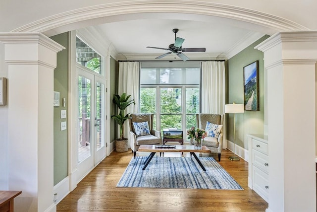 living area featuring crown molding, a ceiling fan, wood finished floors, baseboards, and arched walkways